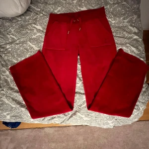 Röda mjukisbyxor från Juicy Couture - Snygga röda mjukisbyxor från Juicy Couture i mjukt material. Byxorna har en bekväm passform med fickor bak och dragsko i midjan. Perfekta för en avslappnad stil.