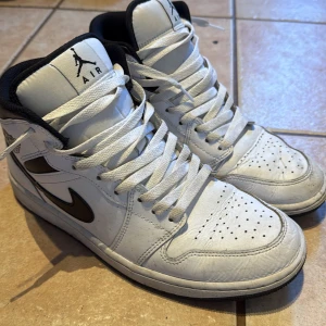 Nike Air Jordans i vitt och svart - Säljer ett par klassiska Nike Air Jordans i vitt med svarta detaljer. Skorna har hög snörning och den ikoniska Air Jordan-loggan på sidan. Perfekta för dig som vill ha en stilren och sportig look.