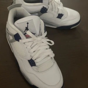 Air Jordan 4 White Midnight Navy - Säljer ett par vita Nike Air Jordans med snygga blå detaljer och snörning. Skorna har en klassisk design med en bekväm passform och är perfekta för sneaker-entusiaster. Den är använd enstaka få gånger och ser fortfarande nya ut.