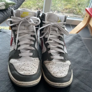 Nike Dunk  - Snygga Nike Dunk sneakers med en cool design. Skorna har en vit bas med grå detaljer och en röd Swoosh på sidan.