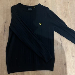 Svart tröja från Lyle & Scott - Snygg svart tröja från Lyle & Scott med deras ikoniska gula logga på bröstet. Tröjan har långa ärmar och en klassisk passform. Perfekt för en stilren look.
