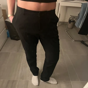 Svarta kostymbyxor - Snygga svarta kostymbyxor med en klassisk design. De har en rak passform och är perfekta för en stilren look. Byxorna knäpps med dragkedja och knappar. De har två fickor fram och sedan en ficka på baksidan 