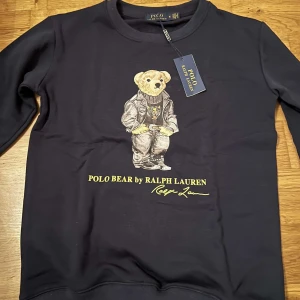 Blå tröja med björntryck från Ralph Lauren - Säljer en blå tröja från Ralph Lauren med ett coolt björntryck på framsidan. Tröjan har långa ärmar och rund halsringning i storlek väldigt stilren tröja  Skriv till mig vid frågor 😇