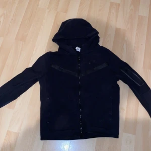 Svart hoodie med dragkedja - Säljer en svart hoodie med dragkedja och huva. Den har långa ärmar och en enkel design som passar perfekt för vardagsbruk. Perfekt för kyliga dagar!