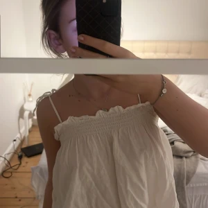 Vit ärmlös linnetopp - Säljer en söt vit linnetopp med smala axelband och volangdetaljer vid halsringningen. Perfekt för varma sommardagar. Toppen har en luftig och bekväm passform. Den e från mango i storlek M men passar mer S , pris kan diskuteras 