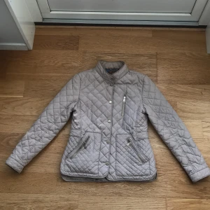Beige quiltad jacka från Zara Girls - Snygg beige quiltad jacka från Zara Girls. Jackan har en dragkedja och knappar framtill samt två fickor med dragkedja. Perfekt för vår och sommar med sin lätta design och stilrena look. Lappen inuti är sliten pga tvätt, se bild. Lite smutsig vid ärm och hals. Säljer för 150kr, är villig att sälja för 100kr.