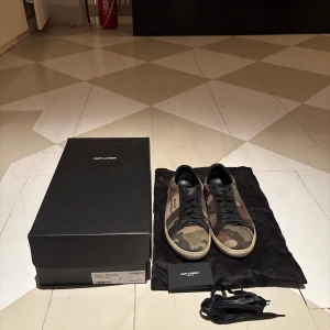 Camouflage sneakers från Saint Laurent - Snygga sneakers från Saint Laurent i ett coolt camouflage-mönster. Skorna har svart snörning och en klassisk design med märkets logga på sidan. Perfekta för en avslappnad stil med en touch av lyx.