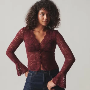 Vinröd spetsblus - Vinröd blus i spets från Ginatricot med v-ringning, knappar framtill och utsvängda ärmslut. Transparent och figurnära modell med långa ärmar och fina spetsdetaljer. 