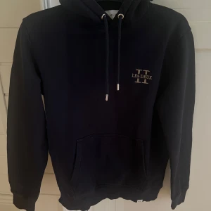 Mörkblå hoodie från Les Deux - Snygg mörkblå hoodie från Les Deux i storlek S. Tröjan har huva med snörning, magficka och diskret logga på bröstet. Tillverkad i mjuk bomull, perfekt för chill dagar. Nypris ca 1200