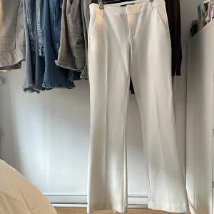 Vita kostymbyxor från Bik Bok LÅGMIDJADE  - Snygga vita kostymbyxor från Bik Bok i storlek 34. Byxorna har en rak och lite vidare passform med klassisk midja och diskreta fickor. Perfekta för en clean och stilren look, matcha med sneakers eller klackar för att höja outfiten.