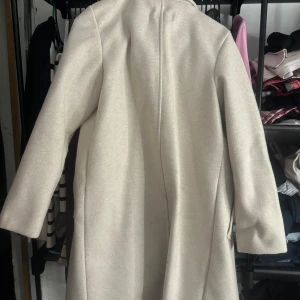 Beige lång kappa från Stradivarius XS - Snygg beige lång kappa från Stradivarius i storlek XS. Klassisk rak modell med krage och två fickor framtill. Inte använd en ända gång