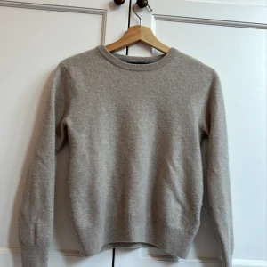 Beige kashmirtröja från Lisa Yang - Superskön beige tröja från Lisa Yang i 100% kashmir. Rund halsringning och ribbade muddar vid ärmslut och nederkant. Perfekt för dig som gillar stilrena och mjuka plagg. Passar dig som vill ha en klassisk look med lyxig känsla.