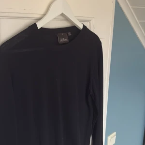 Svart långärmad tröja Oscar Jacobson - Svart långärmad tröja från Oscar Jacobson, tillverkad i Italien. Tröjan är gjord av 100% merinoull och har en klassisk rund hals. Perfekt för dig som gillar stilrena och tidlösa plagg med premiumkänsla.