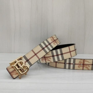 Burberry-inspirerat rutigt bälte - Stilrent bälte med klassiskt Burberry-rutigt mönster i beige, svart och rött. Bältet har en guldig metallspänne med TB-logga och är tillverkat i skinn. Ena sidan är rutmönstrad, andra sidan helsvart med diskret mönster. Perfekt accessoar för att lyfta din outfit.