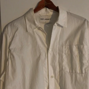 Our Legacy skjorta - Snygg vit skjorta från Our Legacy i klassisk design med krage, bröstficka och knappar framtill. Skjortan är långärmad och har en clean look som funkar till många stilar. Använd men i bra skick. 