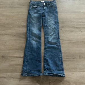 Blå bootcut jeans med fickor där bak. - Säljer ett par blå bootcut jeans med snygga broderade detaljer och knappar på bakfickorna. Jeansen har klassisk femficksdesign och är tillverkade i jeansmaterial med lätt tvättad look. Perfekt för dig som gillar retrovibbar och vill sticka ut lite extra. Storlek 164. Priset kan diskuteras.