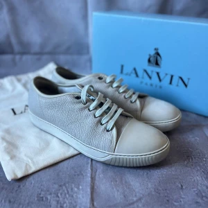 Exklusiva Cap-Toe Lanvin Paris Sneakers – Strl UK 11 / EU 45 – Läder – Med låda & dustbag - Säljer ett par stilrena sneakers från Lanvin Paris. Levereras med original dustbag och låda från Lanvin.  🎨 Färg: Ljusgrå med vit tå och vit yttersula 📏 Storlek: UK 11 / EU 45 📐 Mått: Innermått ca 30 cm (normal passform för EU 45) ♻️ Skick: Bra begagnat skick – mindre bruksspår på sulan, i övrigt välvårdade 🧵 Material: Präglat läder, gummisula, textilfoder och klassiska snören  ‼️Skickas dagen efter köpet genomförs‼️