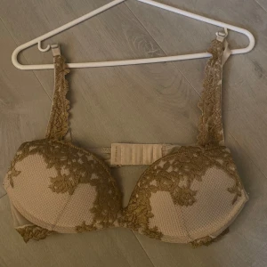 BH från Intimissimi - Supersnygg och populär beige BH från Intimissimi med detaljerad spets i brunt/guld över kuporna och axelbanden.  Säljer då den inte kommer till användning. Den är knappt använd❤️det står ingen storlek men jag tror att det är 75A/80A. Passar även lite större storlek🥰