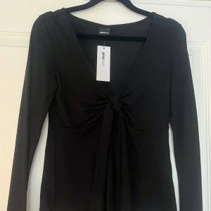 Svart långärmad topp med knyt Gina Tricot - Svart långärmad topp från Gina Tricot med snygg v-ringning och knyt framtill. Modellen är figurnära och har en stilren look som passar till jeans eller kjol. Materialet är mjukt och stretchigt, vilket gör den bekväm att bära hela dagen.