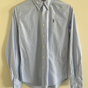 Ljusblå skjorta från Ralph Lauren - Snygg ljusblå skjorta från Ralph Lauren i slim fit-modell. Skjortan har klassisk krage, knappar hela vägen och det ikoniska broderade Polo-logot på bröstet. Inköpt i USA och är storlek 4 vilket motsvarar storlek 36.