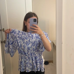 Blåvit zebramönstrad blus från Kappahl  - Säljer en blåvit blus med zebramönster från Kappahl. Blusen har volangdetaljer vid axlarna, resår i midjan för snygg passform och korta puffärmar. Materialet är lätt och luftigt, perfekt för varmare dagar. Supersnygg att matcha med jeans eller kjol!