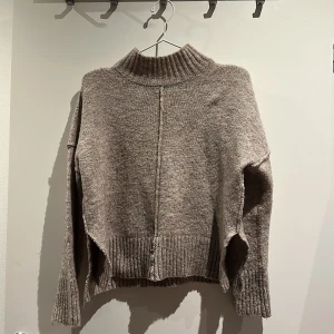 Beige polotröja från ONLY - Säljer en beige polotröja från ONLY i storlek M. Tröjan har ribbad hög krage, ribbade muddar och nederkant samt en snygg söm som går längs mitten fram och bak. Modellen är loose fit med långa ärmar och slits i sidorna. 