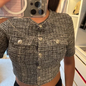 Svartvit croppad blus med knappar - Säljer en croppad blus i svartvitt mönster med korta ärmar och silvriga knappar framtill. Använd 1 gång