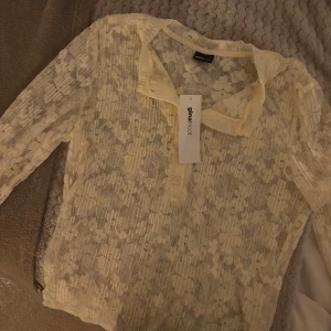 Ljusgul spetsblus från Gina Tricot - Supersöt ljusgul blus från Gina Tricot i transparent spets med plisserade detaljer och liten krage. Blusen har lång ärm och knappar framtill. Perfekt för dig som gillar romantiska vibes och vill sticka ut med en unik topp.