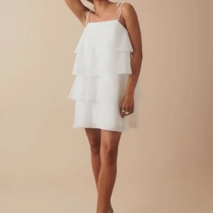 Vit klänning med volanger - Supersöt vit klänning från Gina Tricot med volanger och tunna axelband som knyts. Den har bara kommit till användning en gång så den är i nyskick. Pris kan diskuteras. 