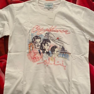 Vit Casablanca t-shirt med tryck - Casablanca t-shirt i vitt med färgstarkt grafiskt tryck framtill som visar personer, byggnader och flygplan. T-shirten har rund hals och korta ärmar. Materialet är mjuk bomull och passformen är normal. Perfekt för dig som gillar unika prints och streetstyle.