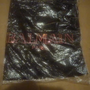 Svart Balmain Paris t-shirt - Svart t-shirt från Balmain Paris med stort metallicrosa tryck på bröstet. Klassisk rund hals och korta ärmar. Snygg och stilren design som ger en lyxig vibe. Perfekt för dig som gillar exklusiva märken och vill sticka ut med en statement-logga. MotherFUCK vad grym öjuseffekt det blir på loggan då man dansar sig igenom ett hav av människor på krogen