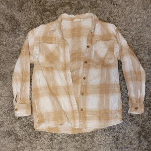 Beige och vit rutig skjorta KappAhl - Snygg rutig skjorta från KappAhl i beige och vitt. Skjortan har långa ärmar, två bröstfickor och knappar framtill. Materialet är mjukt och känns skönt mot huden.