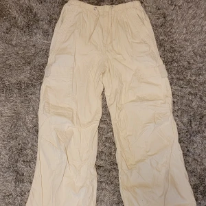 Beiga cargopants med snörning XXS - Säljer ett par beiga cargopants i storlek XXS med snörning i midjan och stora sidofickor. Byxorna har en loose passform och är tillverkade i bomull, perfekta för en chill och avslappnad stil. Ett snöre på ena benet saknas, se bild 2, men det är lätt att fixa. 