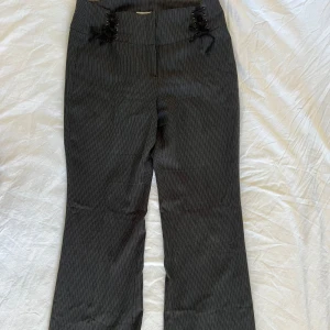Svarta bootcut byxor från Naf Naf - Snygga svarta bootcut byxor från Naf Naf med diskreta vita ränder och cool snörningsdetalj i midjan. Byxorna har hög midja och är gjorda i ett mjukt bomullsmaterial med lite stretch. Perfekt för dig som gillar en trendig och bekväm look. Står storlek 38 men är 36 själv och de är ganska små. Hade sagt de är mer xs. 