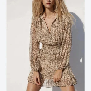 Leopardmönstrad kortklänning med volang - Säljer en superfin kortklänning med leopardmönster och volangkant. Klänningen har långärmade, transparenta ärmar och smock i midjan för en snygg passform. V-ringad hals och lätt, luftig känsla. Perfekt för dig som vill sticka ut med coola detaljer.