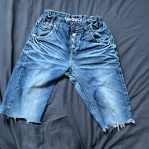 Lab Industries blå jeansshorts - Säljer ett par blå jeansshorts från Lab Industries med loose passform och råa, fransiga benslut. Shortsen har klassiska fem fickor, knappgylf och elastisk midja med logotypdetalj. Perfekta för chill dagar och streetstyle.