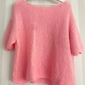 Ljusrosa stickad tröja med kort ärm - Supermysig ljusrosa stickad tröja med korta ärmar och rund hals. Tröjan har en loose passform och är gjord i ett fluffigt material som känns riktigt skönt mot huden. Perfekt för dig som gillar en chill och söt stil.