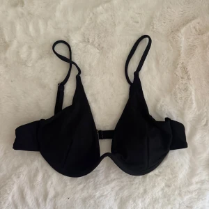 Svart ribbad bikiniöverdel L - Snygg svart bikiniöverdel med ribbad struktur och justerbara axelband. Modellen har bygel och knäppe bak för extra stöd. Tillverkad i mjuk och stretchig polyesterblandning med 18% spandex för skön passform. Perfekt för strandhäng och poolparty!