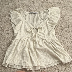 Vit blus med volang från 157 - Supersöt vit blus från 157 i storlek S. Blusen har volangärmar, v-ringning med knyt framtill och ett flowigt, lätt rynkat tyg som ger en chill och feminin vibe. Perfekt till jeans eller kjol när du vill ha en romantisk look.