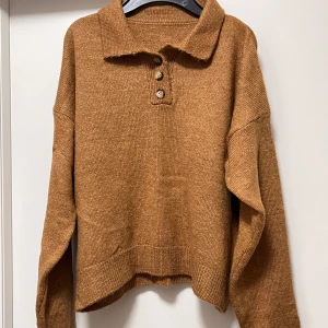 Brun stickad pikétröja med knappar - Säljer en brun stickad pikétröja med krage och tre snygga knappar framtill. Tröjan har långärmad design och är lite loose i passningen, perfekt för dig som gillar chill och enkel stil. Materialet är mjukt och skönt mot huden.