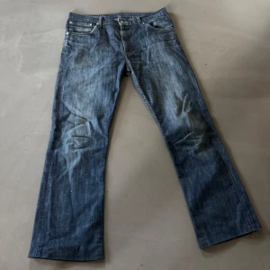 Levi's 507 blå bootcut jeans W34 L34 - Säljer ett par klassiska Levi's 507 jeans i blå tvätt med bootcut passform. Jeansen har fem fickor, knappgylf och snygga slitningar för en cool look. Perfekta för dig som gillar lite bredare ben och tidlös denimstil. Jeansen är uppsydda och är kortare än 34!
