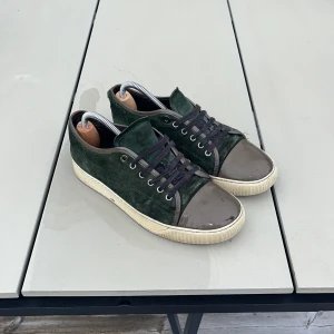 Mörkgröna sneakers med mocka och lack - Snygga mörkgröna sneakers med ovandel i mocka och lackad tå i brunt. Skorna har svarta snören och en vit platt sula som ger en cool kontrast. Perfekta för dig som gillar stilrena detaljer och vill sticka ut med en unik färgkombination.