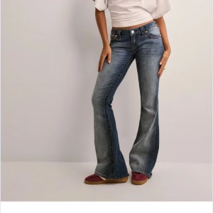 Blå bootcut jeans från True Religion - Snygga blå jeans från True Religion med bootcut passform och låg midja. Jeansen har klassisk femficksdesign, markerade sömmar och ikoniska broderade bakfickor. Materialet är slitstarkt denim i bomull med en tvättad look och lätt faded effekt.