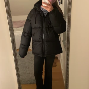 Svart pufferjacka från H&M XS - Säljer en svart pufferjacka från H&M i storlek XS. Jackan har en oversized look, huva och dragkedja framtill. Perfekt för kalla dagar med sin fluffiga och quiltade design. Passar dig som gillar streetstyle och vill hålla dig varm under vintern.