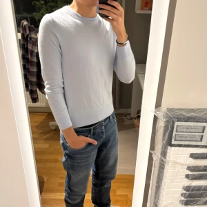 Ljusblå stickad tröja herr - Snygg ljusblå stickad tröja med rund hals och lång ärm. Perfekt för dig som gillar en clean och enkel stil. Tröjan har en normal passform och är gjord i mjukt material som känns skönt mot huden. Passar till jeans eller chinos för en chill look.