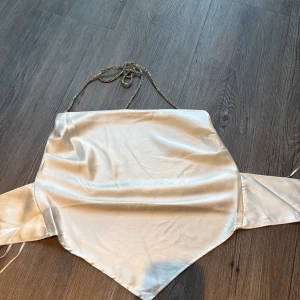 Champagnefärgad satin tubtopp Gina Tricot - Säljer en snygg champagnefärgad tubtopp från Gina Tricot i glansig satin. Toppen har bandeau-modell med smala, glittriga axelband och knyt i ryggen. Perfekt för dig som vill ha en trendig och stilren look med lite extra shine.