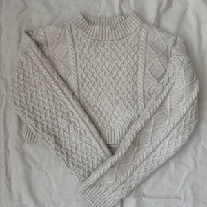 Croppad stickad tröja från H&M - Säljer en croppad stickad tröja från H&M i ljus beige färg. Tröjan har ett flätmönster, ribbad hals och muddar samt långa ärmar. Pris kan diskuteras 