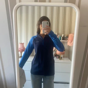 Blå fleece-tröja från Columbia - Mörkblå fleece-tröja från Columbia med ljusblå ärmar och half zip framtill och logga på bröstet.