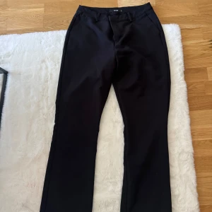 Svarta kostymbyxor från Bik Bok - Snygga svarta kostymbyxor från Bik Bok i klassisk rak modell med midwaist. Byxorna har bälteshällor, sidfickor och en diskret bakficka. Materialet är mjukt och har en lätt stretch för extra komfort. Perfekta för en clean och stilren look. Något små i storleken.