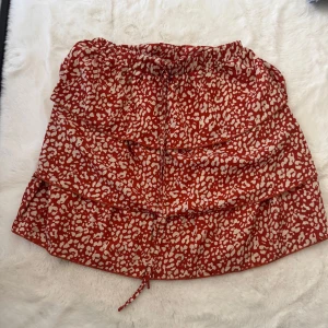 Röd leopardmönstrad kjol från SHEIN - Supersöt röd kortkjol från SHEIN med beige leopardmönster och volanger. Kjolen har elastisk midja och snörning framtill för extra detalj. Perfekt för dig som gillar trendiga prints och vill sticka ut lite extra.